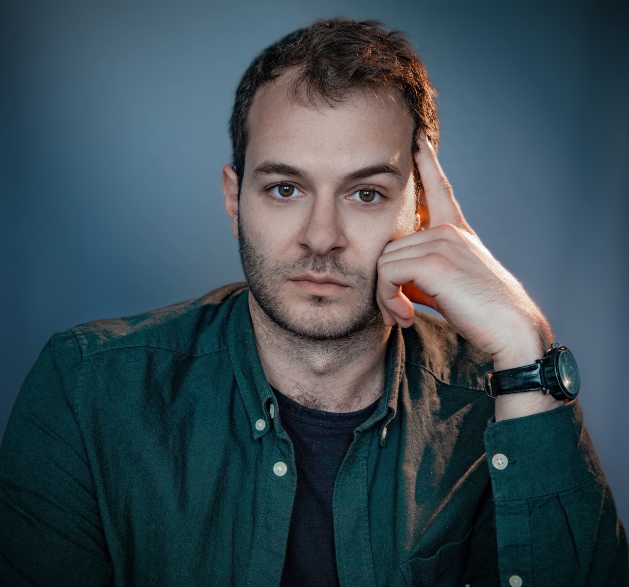 Portrait en chemise verte, la main contre la tempe, sur fond bleu