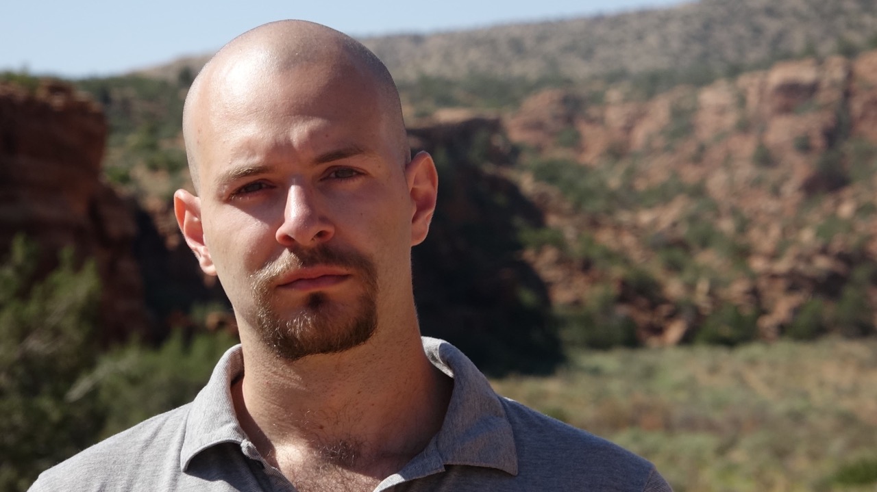 Crâne rasé et barbe, en extérieur devant un canyon rocheux