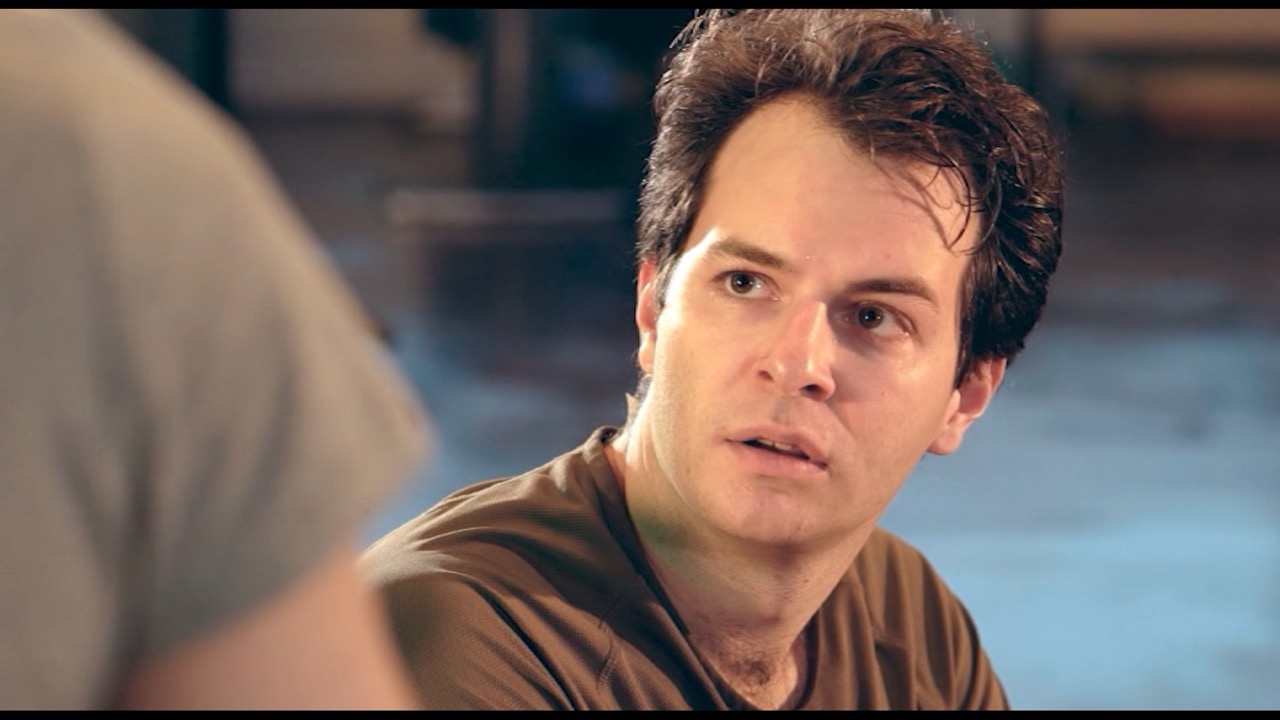 Image de film : gros plan en tee-shirt marron, regard inquiet vers un interlocuteur