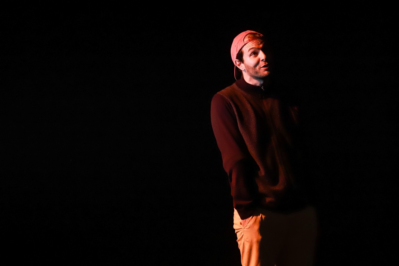 Seul en scène dans un halo de lumière, casquette rouge et pull bordeaux